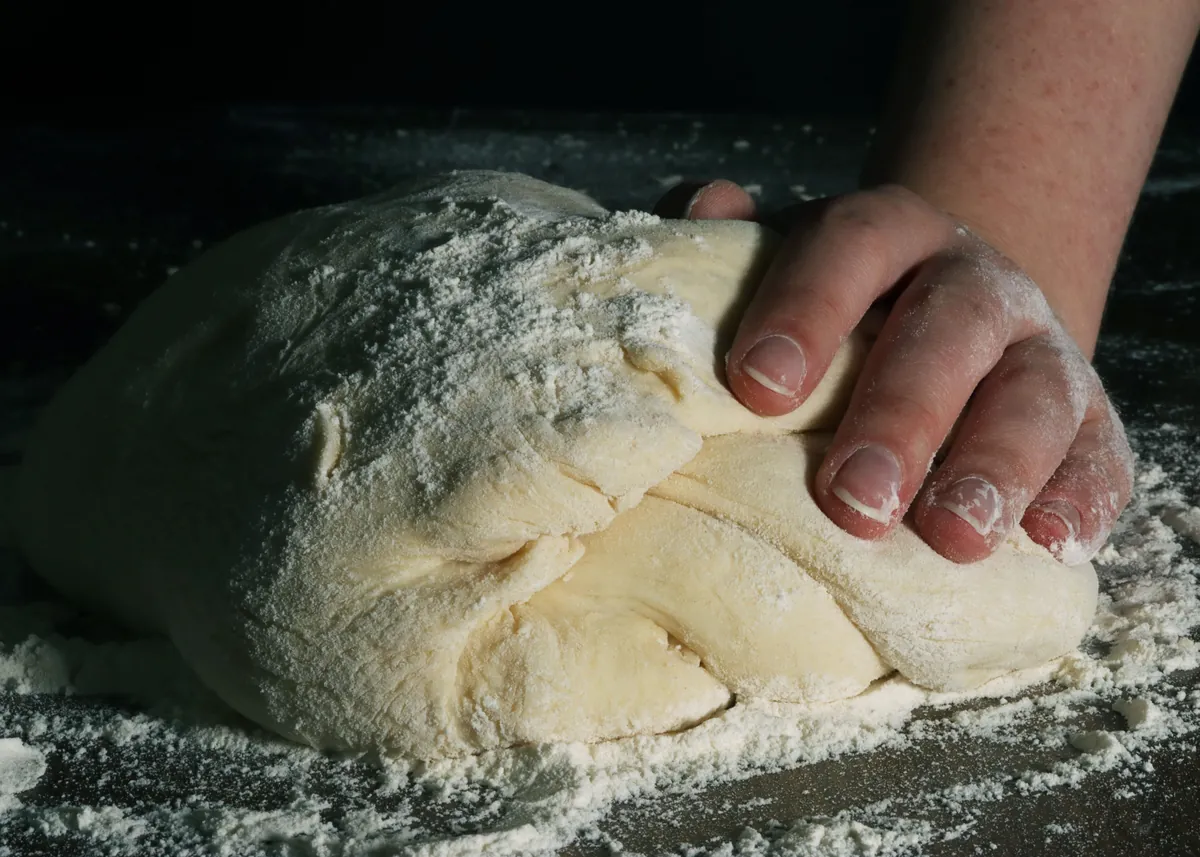 Baker's hands kneading floured dough on a dark workbench