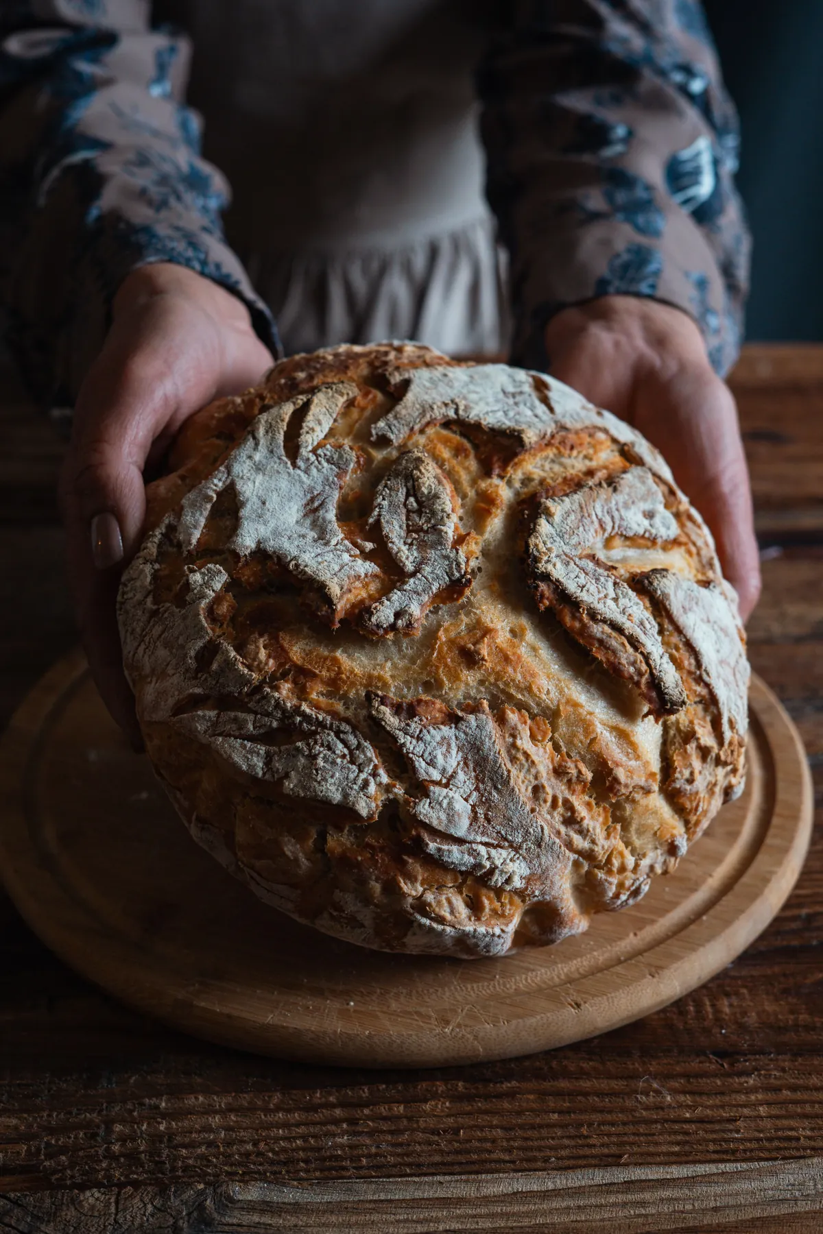 Baker presenting a crusty boule over the wooden counter